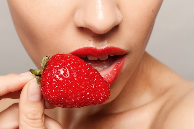 Mulher com lábios vermelhos comendo morango