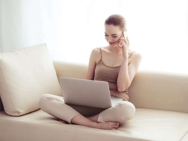 Mulher com laptop e smartphone móvel no sofá trabalhando sozinha em casa