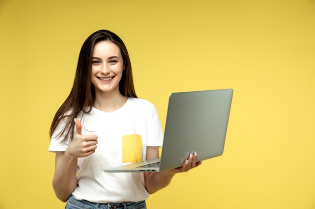 Mulher com laptop em fundo amarelo, mostrando os polegares para cima símbolo