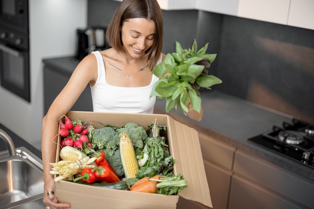 Mulher com legumes frescos embalados em caixa de papelão na cozinha