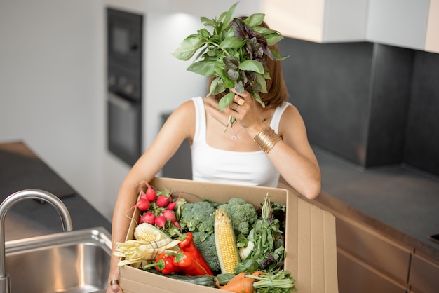 Mulher com legumes frescos embalados em caixa de papelão na cozinha
