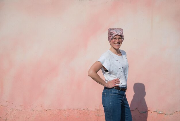 Mulher com lenço rosa lutando contra o câncer em uma parede colorida