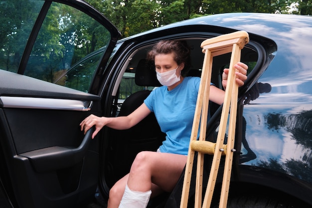 Mulher com lesão na perna entra no carro Gesso ortopédico muletas ortopédicas