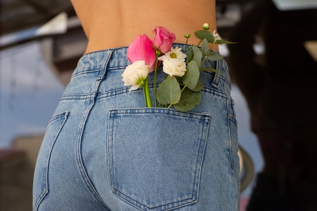 Mulher com lindas flores delicadas no bolso de trás da calça jeans Mulher apunhala de volta para a câmera Um pequeno buquê de flores do campo no bolso de trás