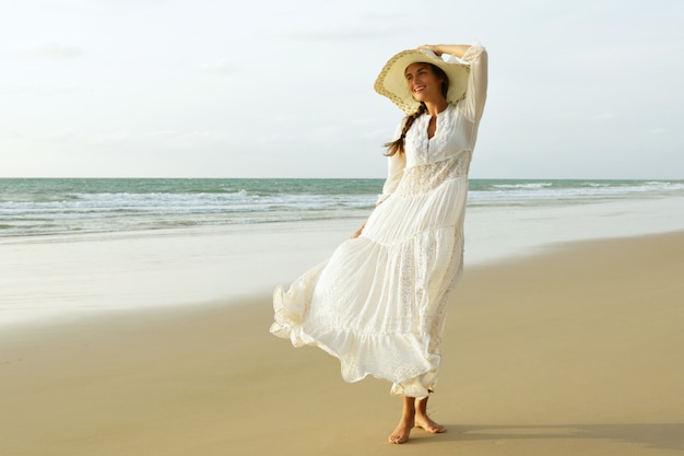 Mulher com lindo vestido branco está caminhando na praia durante o pôr do sol