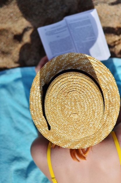 Mulher com livro usando chapéu na praia