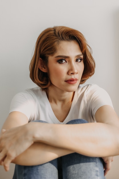 Mulher com look descolado de camiseta branca e jeans relaxando no quarto do apartamento