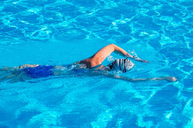 Mulher com maiô nadando em uma piscina de água azul. Esporte.