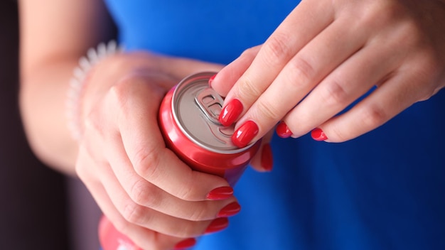 Mulher com manicure vermelha abrindo lata de ferro com bebida fechada