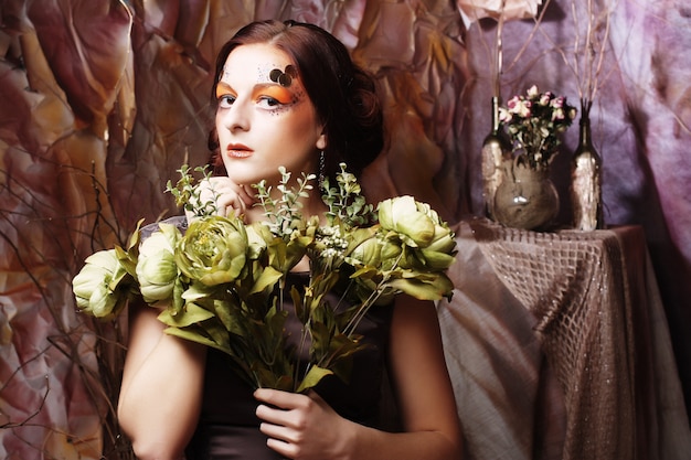 Mulher com maquiagem criativa brilhante segurando flores verdes