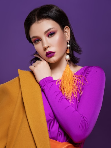 mulher com maquiagem de cor brilhante em um vestido roxo e casaco amarelo