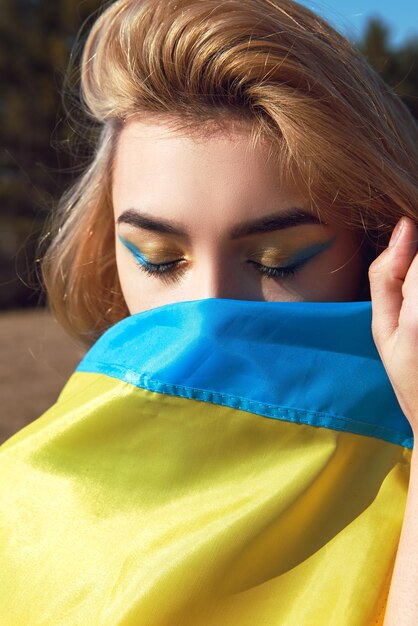 Foto mulher com maquiagem patriótica embrulhada na bandeira ucraniana fique com o conceito da ucrânia