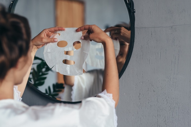 Mulher com máscara de lençol nas mãos no banheiro antes de aplicá-la no rosto.