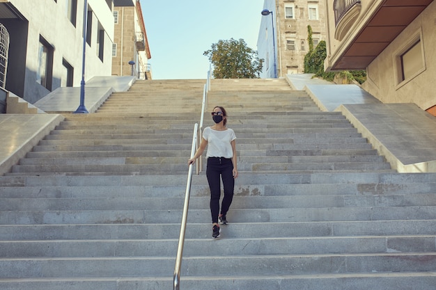 Mulher com máscara descendo escadas em uma cidade