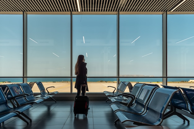 Mulher com máscara e mala na sala de embarque do aeroporto