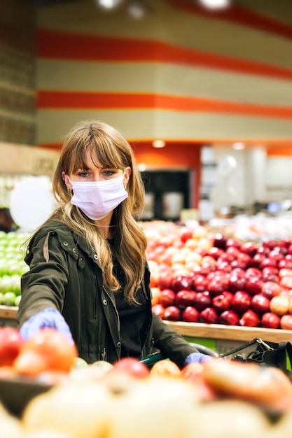 Mulher com máscara facial usando luvas de látex enquanto fazia compras em um supermercado durante a quarentena de coronavírus