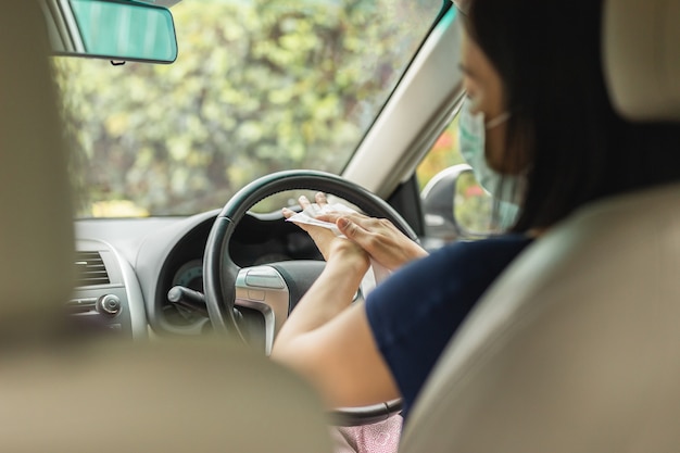 Mulher com máscara médica limpando as mãos com lenços umedecidos enquanto está sentada no carro