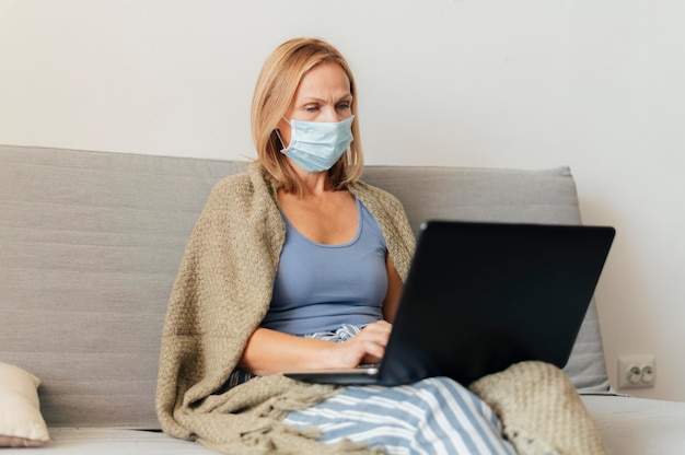 Mulher com máscara médica trabalhando em um laptop em casa durante a quarentena