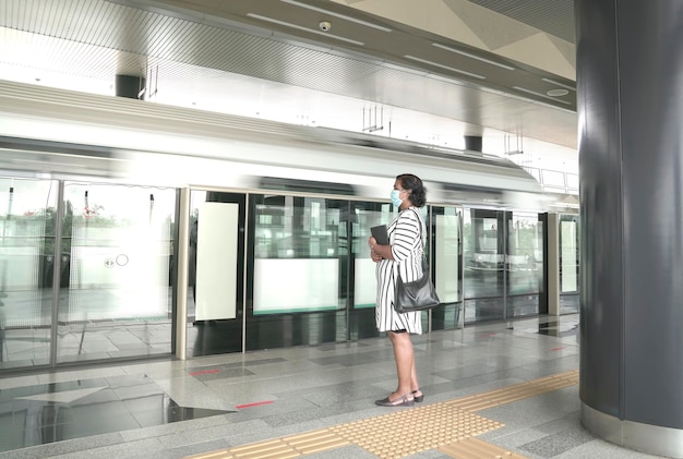 Mulher com máscara na espera de trem na plataforma de uma estação de metrô