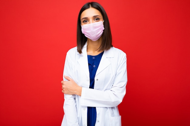 Mulher com máscara protetora de vírus no rosto contra coronavírus e jaleco branco médico isolado no fundo.