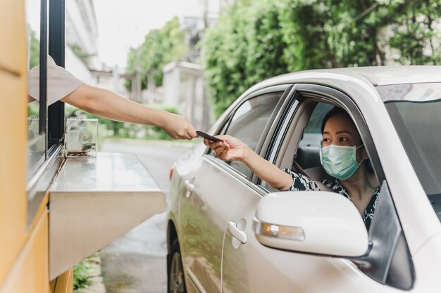 Mulher com máscara protetora pagando fast food com cartão de crédito do carro dela