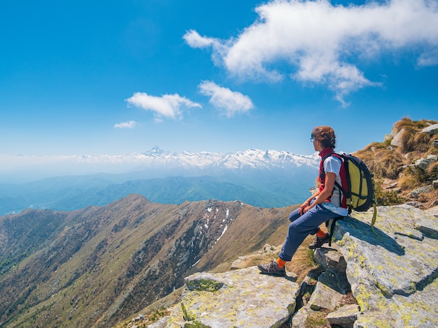 Mulher com mochila descansando no topo da montanha, olhando a paisagem dramática da atividade de verão no vale