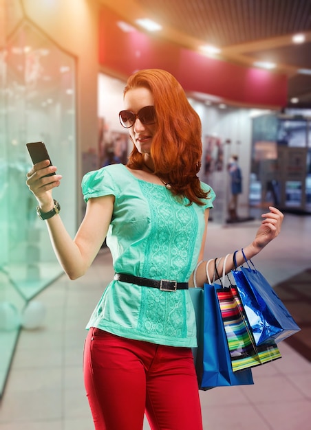 Mulher com muitas bolsas de atirar usando o telefone no shopping