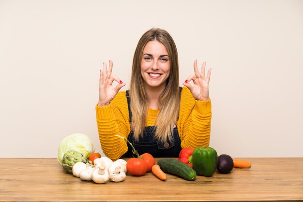 Mulher com muitos legumes, mostrando um sinal de ok com os dedos