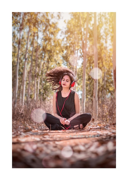 Foto mulher com o cabelo desarranjado ouvindo música enquanto está sentada contra as árvores na floresta