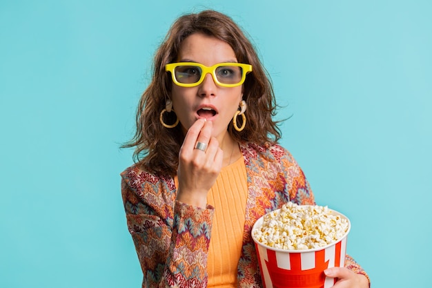 Mulher com óculos 3D comendo pipoca e vendo interessante série de televisão, esportes, jogos, filmes, filmes online.