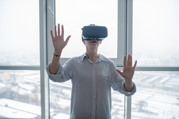 Mulher com óculos de realidade virtual parada em frente a uma grande janela