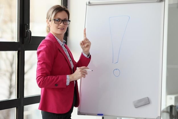 Mulher com óculos fica ao lado do quadro branco com um grande ponto de exclamação desenhado, o treinador de negócios paga