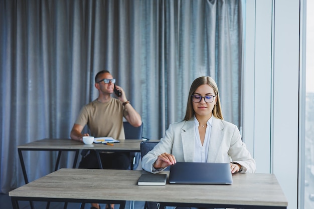 Mulher com óculos na mesa enquanto trabalhava com colegas no escritório Conceito de empresários bem sucedidos modernos Homem e mulher sentados em mesas de madeira