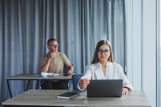 Mulher com óculos na mesa enquanto trabalhava com colegas no escritório conceito de empresários bem sucedidos modernos homem e mulher sentados em mesas de madeira