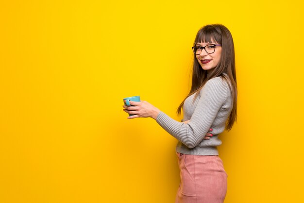 Mulher, com, óculos, sobre, parede amarela, segurando, um, xícara quente café