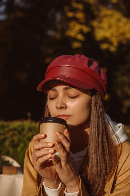 Mulher com olhos fechados desfrutando de cheiro aromático de café em copo de papel para viagem em dia ensolarado no parque
