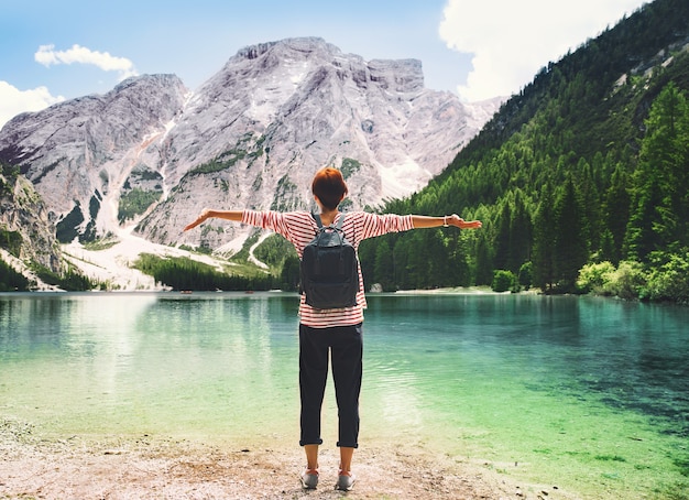 Mulher com os braços erguidos, olhando para o Lago Braies com montanhas ao fundo