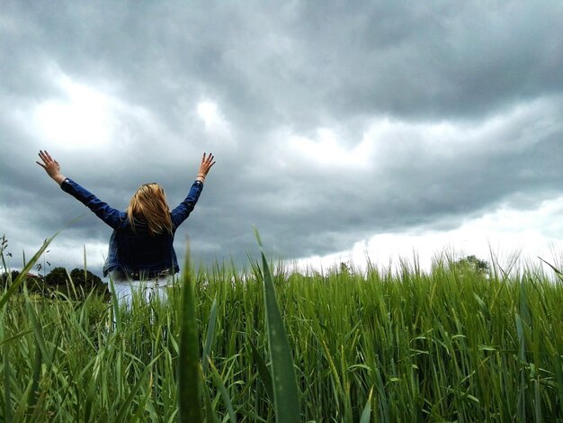 Foto mulher com os braços levantados de pé no campo contra o céu nublado