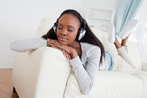 Mulher com os olhos fechados, desfrutando de música no seu sofá