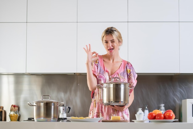 Mulher com panela fica perto da mesa na cozinha em casa dona de casa cozinhando na cozinha no