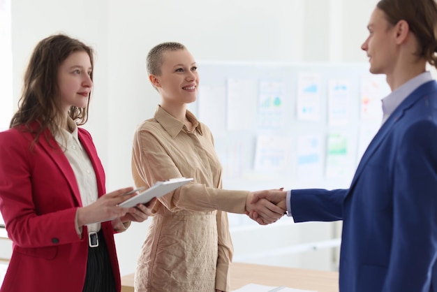 Mulher com prancheta observa colegas apertando as mãos no escritório moderno funcionários felizes fazem