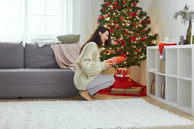 Mulher com presente na caixa de presente perto da árvore de Natal em casa