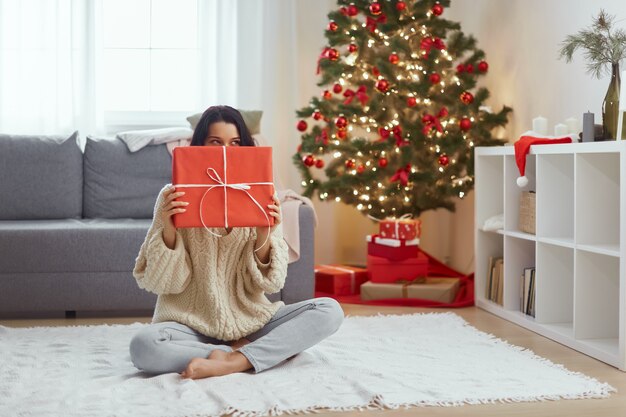 Mulher com presente na caixa de presente perto da árvore de Natal em casa