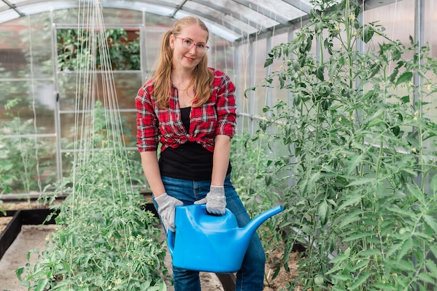 Mulher com regador de jardim rega plantas e tomates verdes jardinagem e conceito de estufa