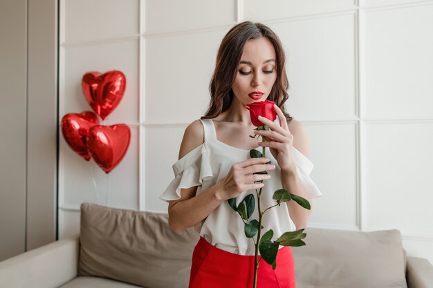 Mulher com rosa vermelha em casa com balões vermelhos em apartamento moderno