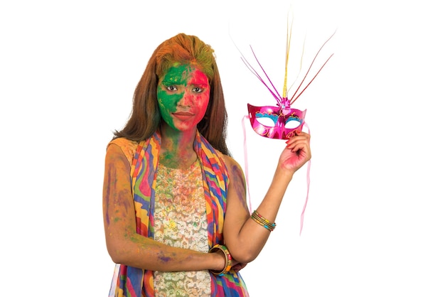 mulher com rosto colorido, segurando a máscara de carnaval e celebrando o holi.