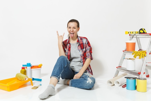 Mulher com roupas casuais com chifres gesto no chão com instrumentos para sala de apartamento de renovação isolado no fundo branco. Papel de parede, acessórios para colar, ferramentas de pintura. Conceito de reparação.