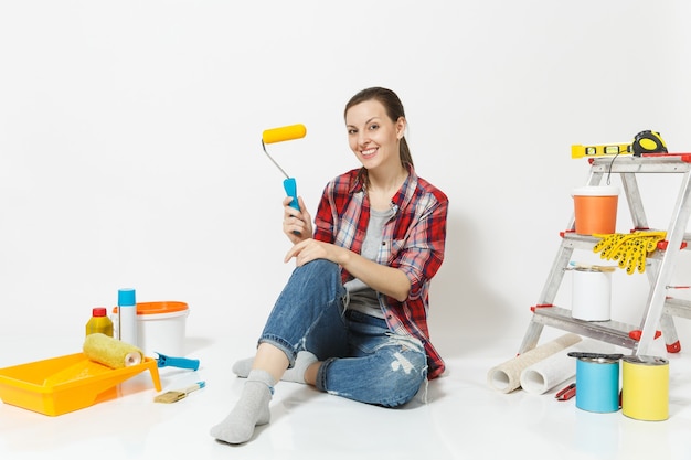 Mulher com roupas casuais, sentada no chão com o rolo de pintura, instrumentos para apartamento de renovação isolado no fundo branco. papel de parede, acessórios para colar, ferramentas de pintura. conceito de casa de reparo.