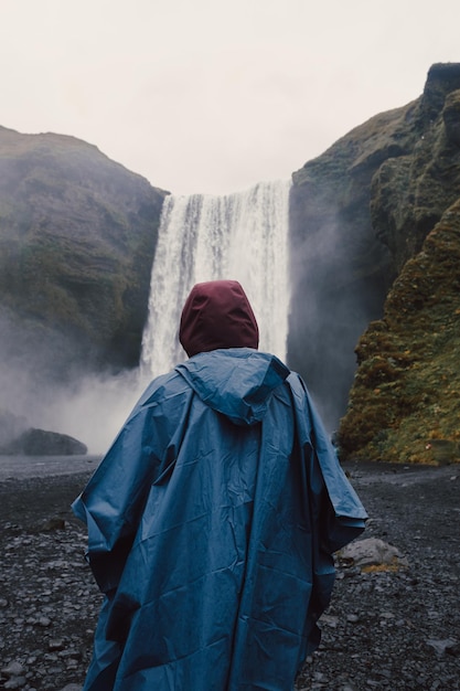 Mulher com roupas de chuva na frente da cachoeira Skogafoss na Islândia durante um dia mal-humorado Viajar no conceito de van estilo de viagem Visite a Islândia e o conceito de países do norteCopiar imagem do espaço