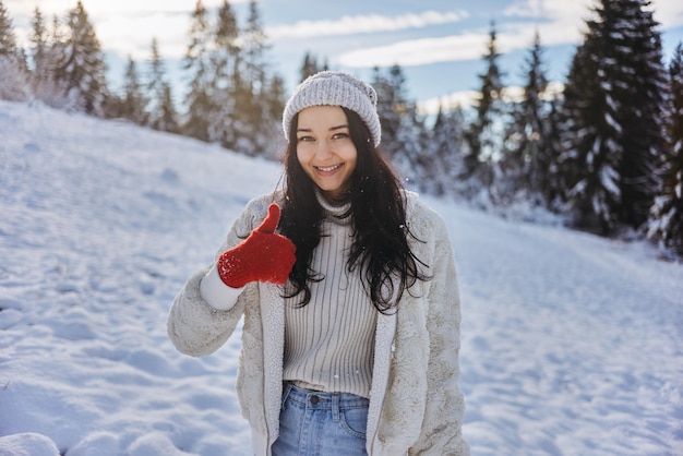 Mulher com roupas de inverno com os polegares levantados na frente de uma floresta de montanha ao ar livre